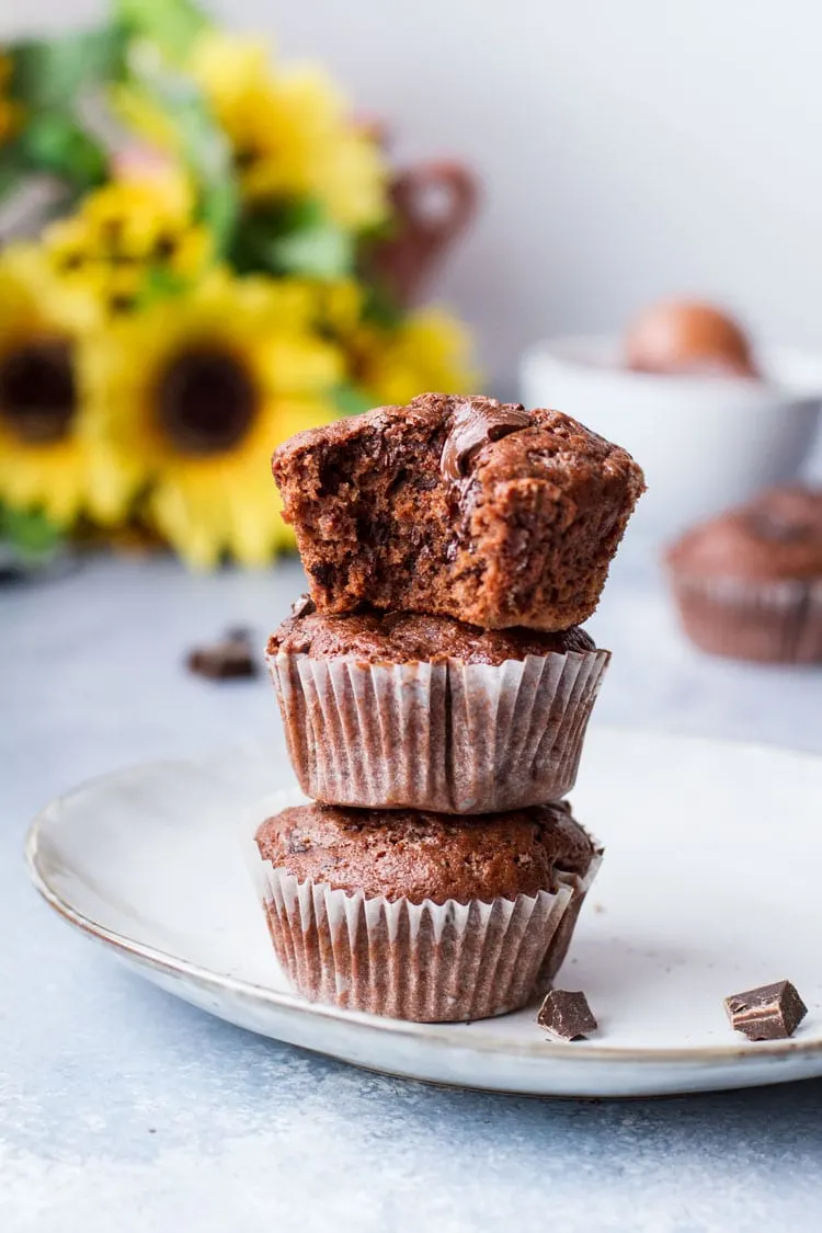 Three chocolate muffins stacked on top of each other, the top one is taken a bite out of.