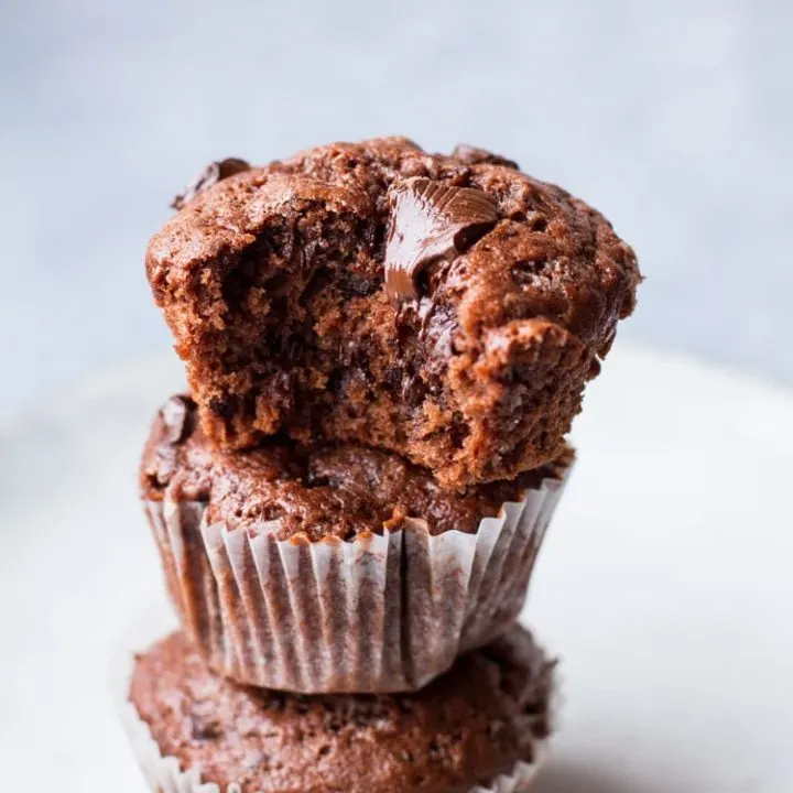 Three banana muffins stacked on each other, one taken a bite out of and chocolate is melting on top.