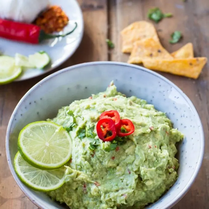 A rustic bowl filled with guacamole and garnished with lime and chili. Square recipe photo.