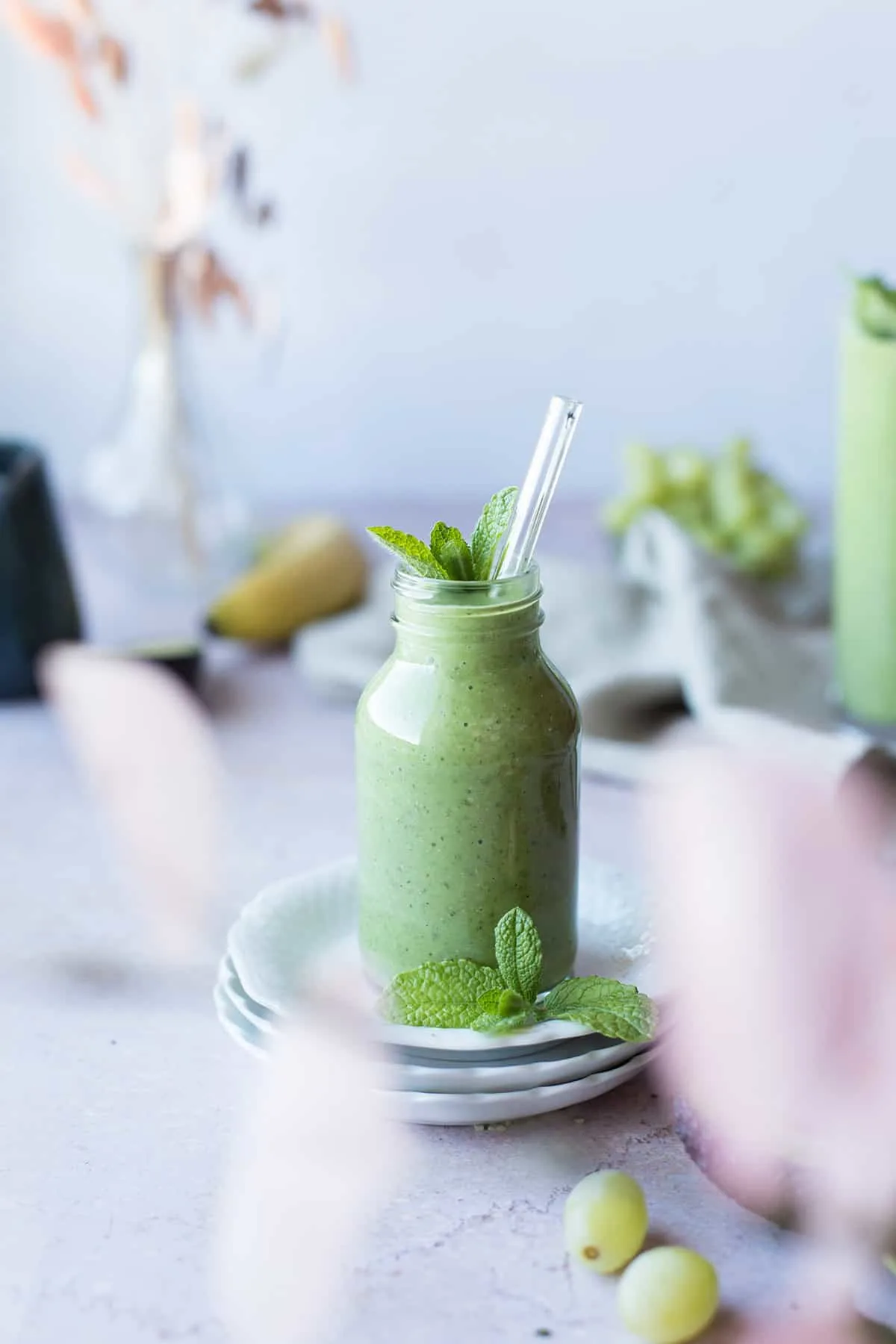 A small glass with green avocado smoothie, with a glass straw.