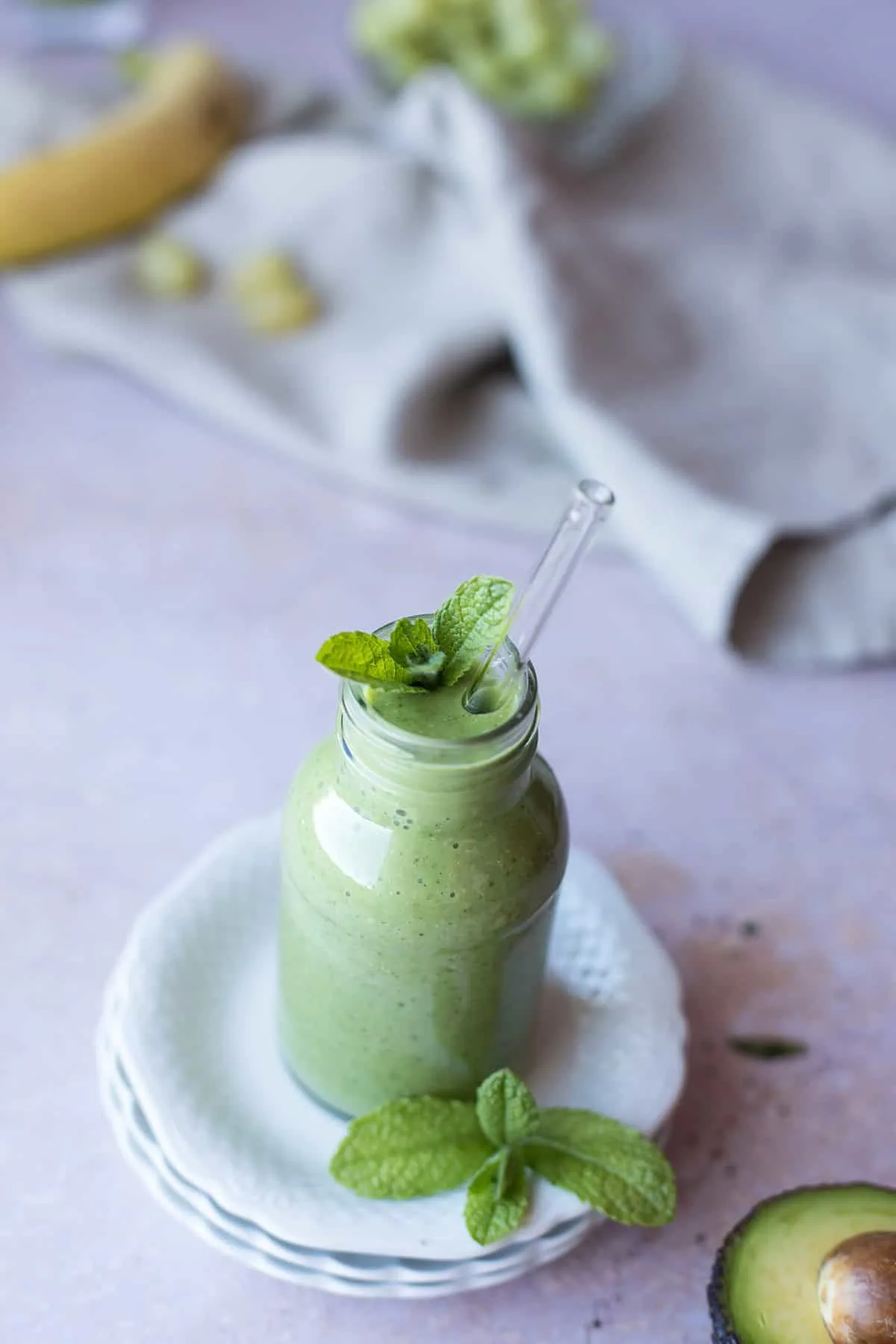 A small glass bottle with green smoothie on top of a vintage plate.