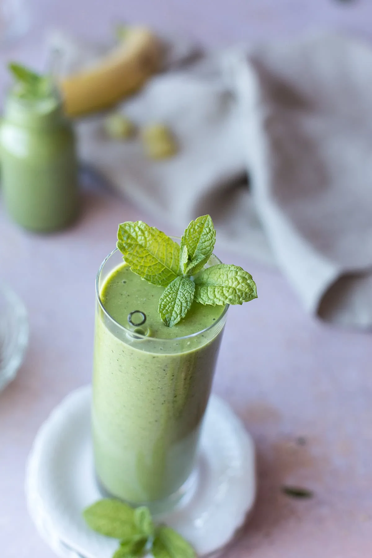 Focus point on a fresh mint in a tall glass of green grape smoothie.