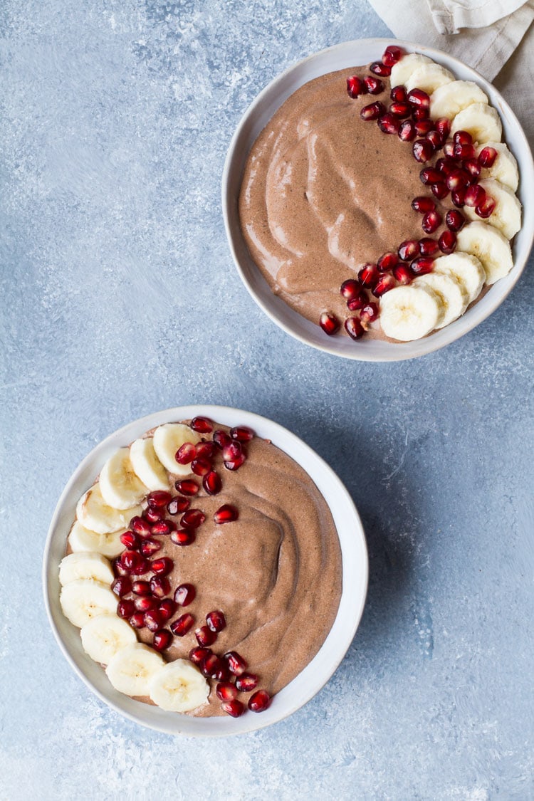 Two bowls with chocolate pudding and banana slices and pomegranate seeds.