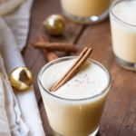 A glass with homemade eggnog with a cinnamon stick floating on the foam.