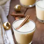 A glass with homemade eggnog with a cinnamon stick floating on the foam.