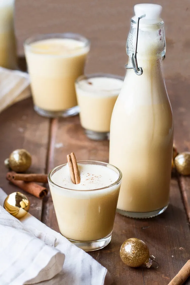 A glass and a small bottle of eggnog. Glass garnished with cinnamon stick.