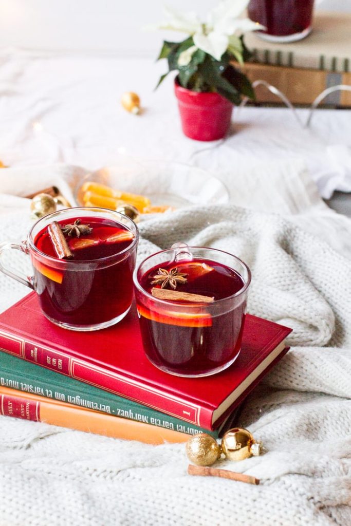Two glass mugs with mulled wine on top of three old books, white background.