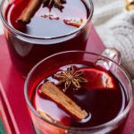 Two mugs with mulled wine garnished with cinnamon stick, star anise and clementine slice.