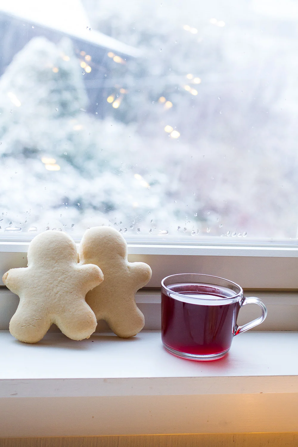 Two Christmas Men cookies in the window sill with a glass mug with mulled wine.