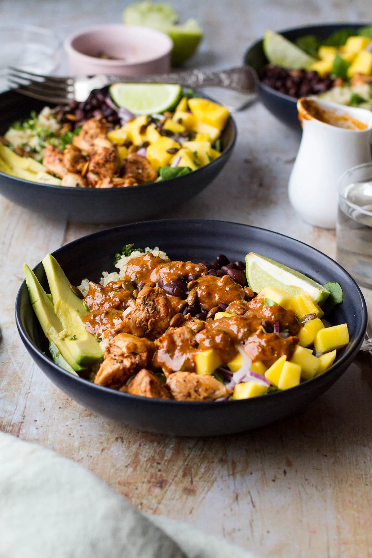 Black bowl with quinoa and lime chicken, beans and mango.