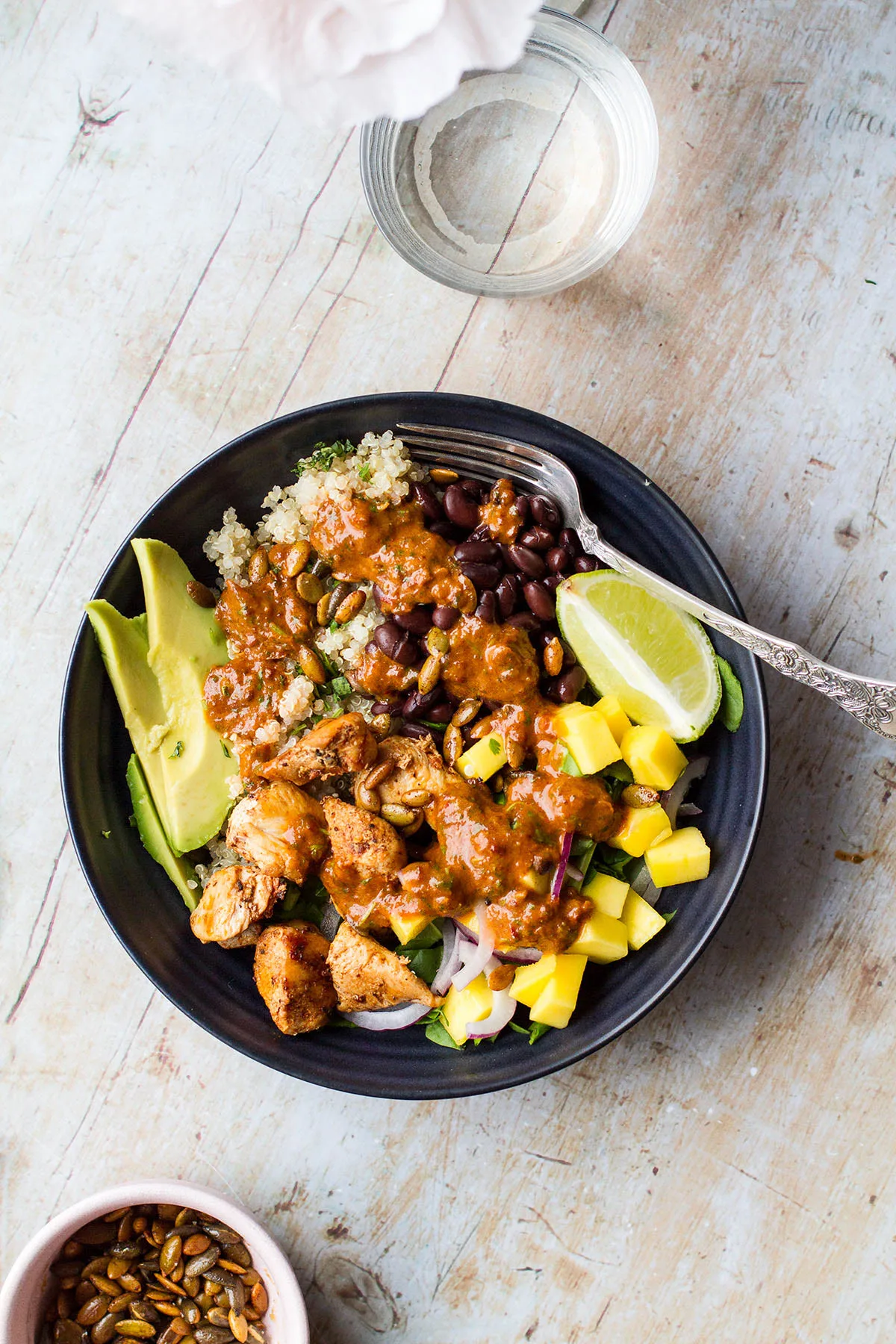 One black bowl filled with quinoa, lime chicken, mango, avocado and chipotle sauce.