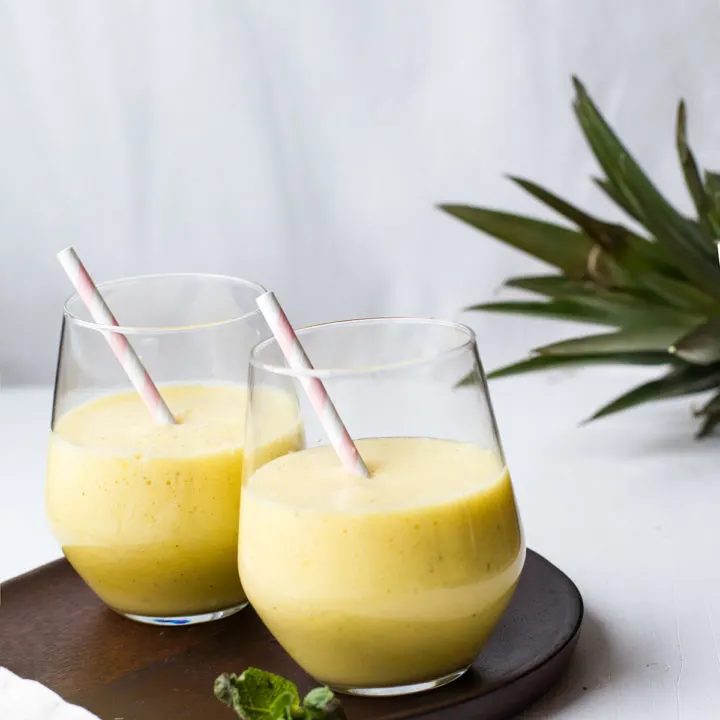 Two glasses with a yellow smoothie on a wooden plate.