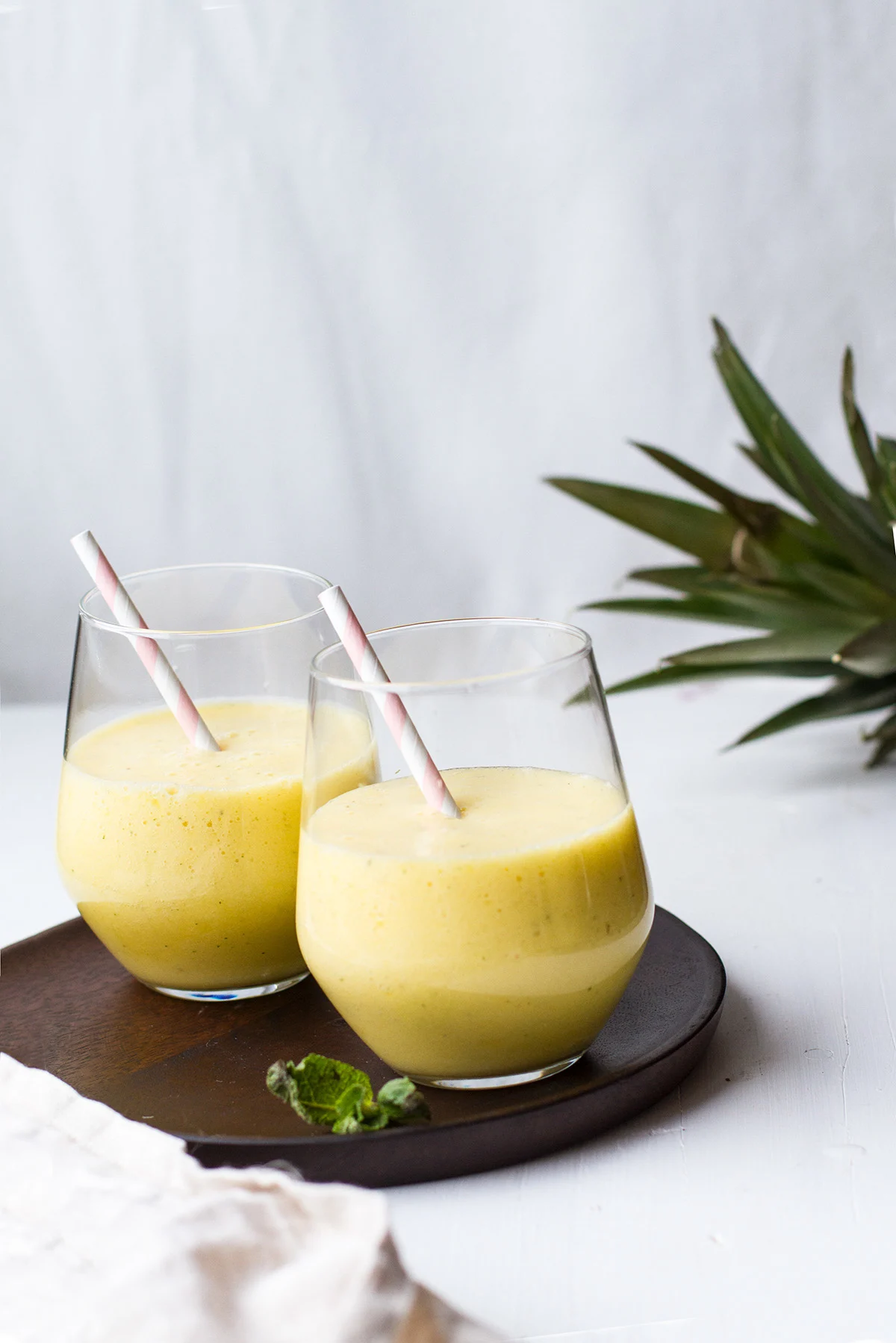 Two glasses with a yellow smoothie on a wooden plate.