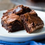Three brownies stacked on a white plate, blue towel.