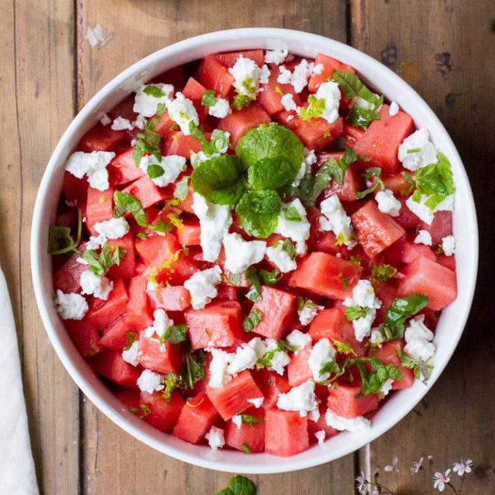 Watermelon salad in a white bowl on a wooden table, flatlay. Square photo.