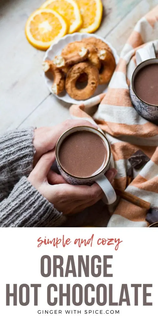 Hands holding a cup of orange hot chocolate. Donuts in the background. Pinterest pin.