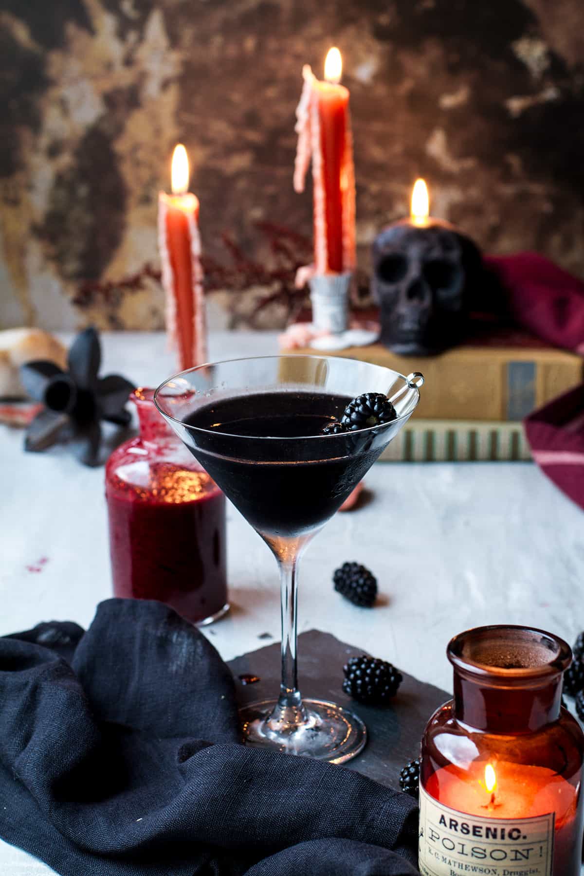 Black martini Halloween cocktail with dark skull candle and orange candles in the background.