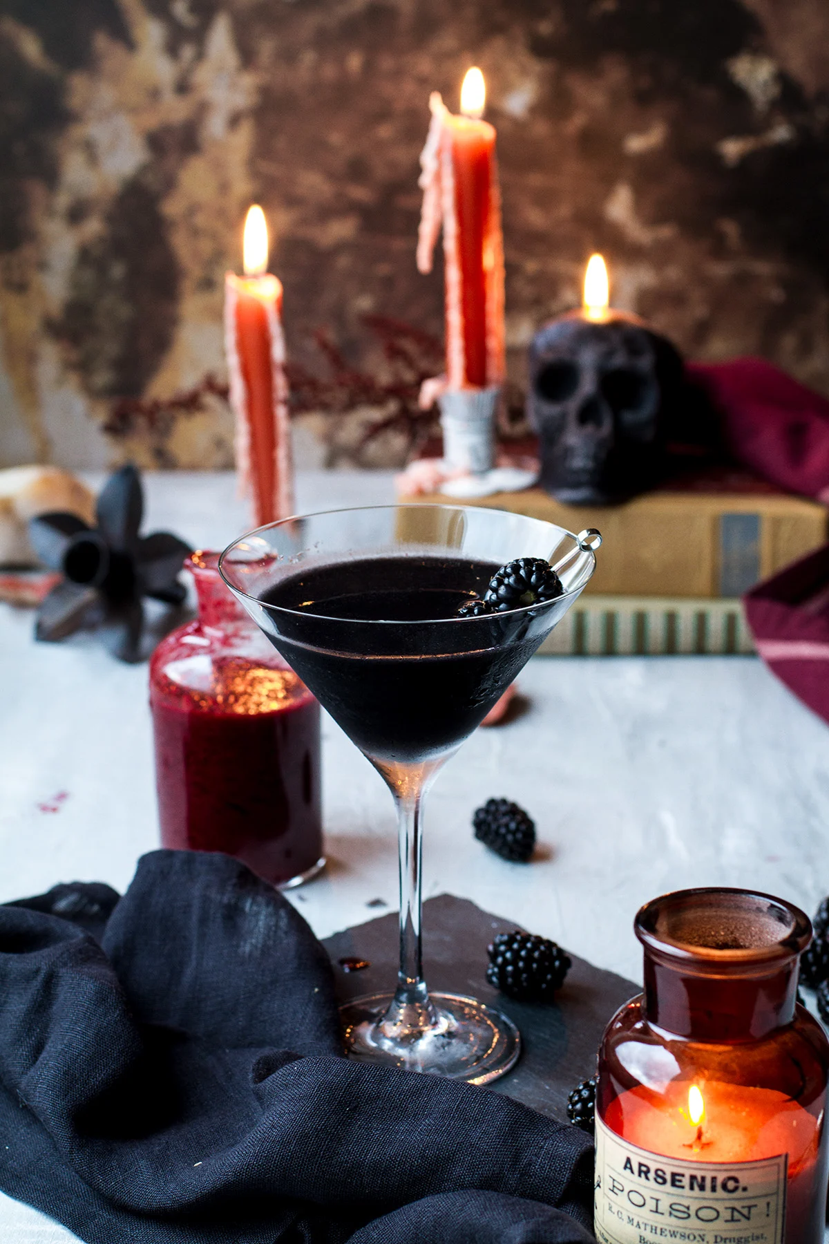 Black martini Halloween cocktail with dark skull candle and orange candles in the background.