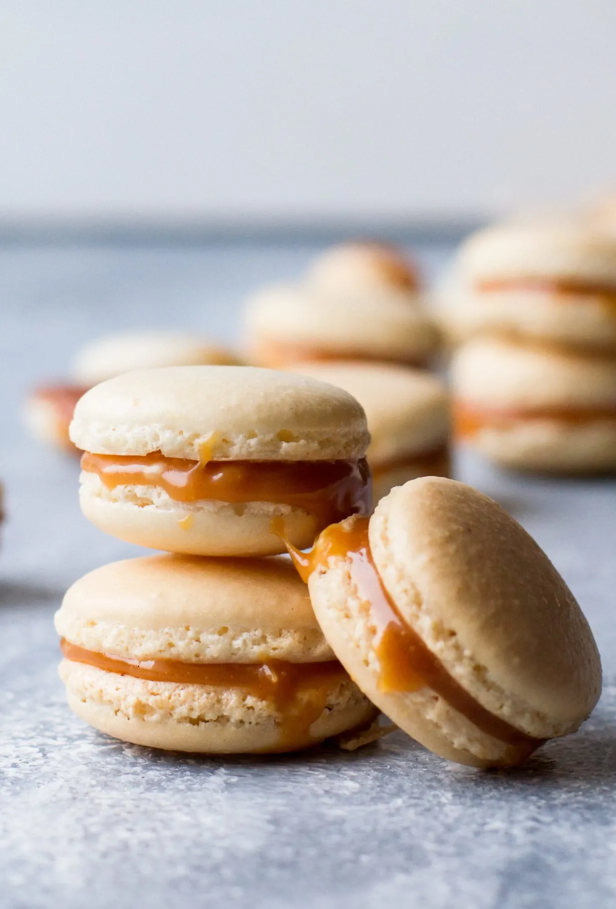 Salted Caramel Macarons with Homemade Caramel stacked with blurred macarons in the background.