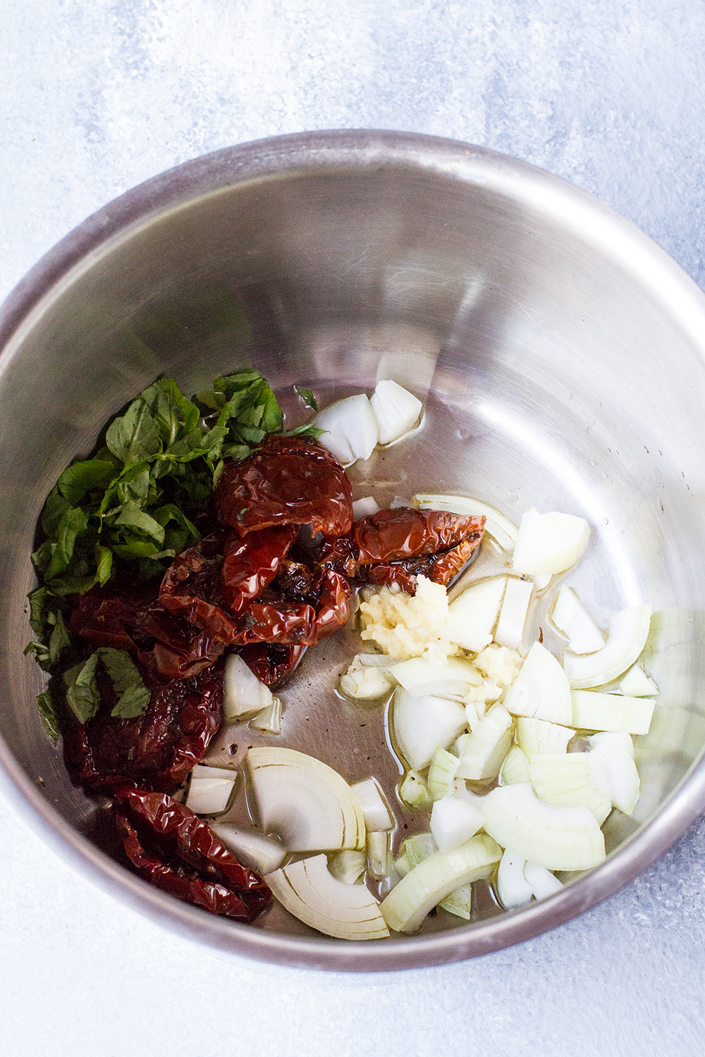 A saucepan with sun-dried tomatoes, onion and herbs.