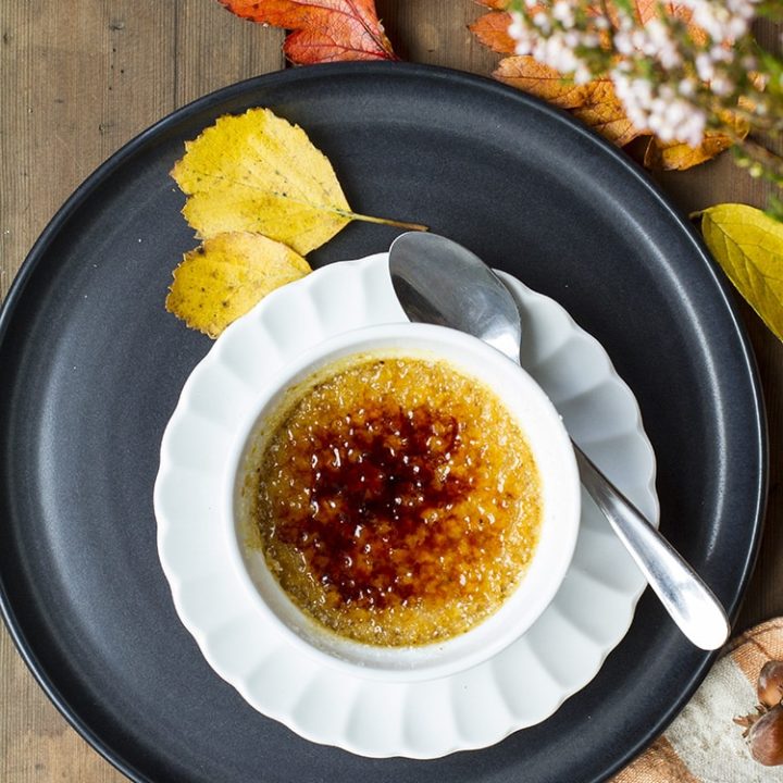 Pumpkin creme brulee on a small white plate on a bigger black plate. Leaves scattered around.
