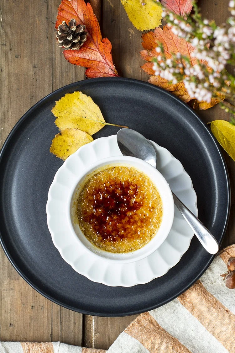 Pumpkin creme brulee on a small white plate on a bigger black plate. Leaves scattered around.