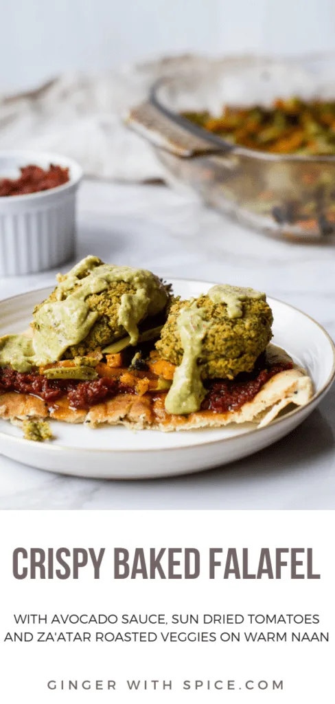 A naan with sun-dried tomatoes paste, roasted vegetables baked falafel patties and avocado sauce on a white plate and white marble background. Pinterest pin