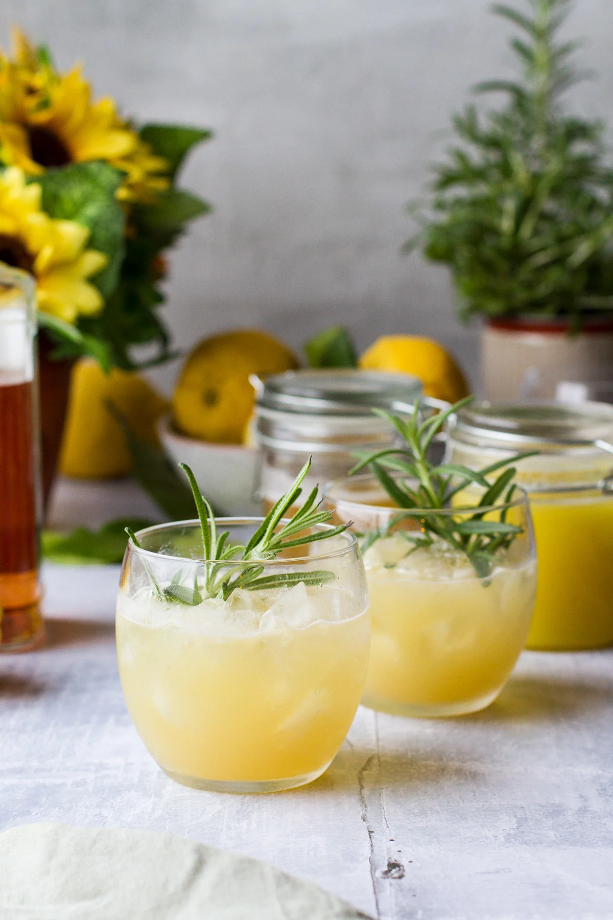 Two round glasses with a yellow whiskey drink, garnished with rosemary.