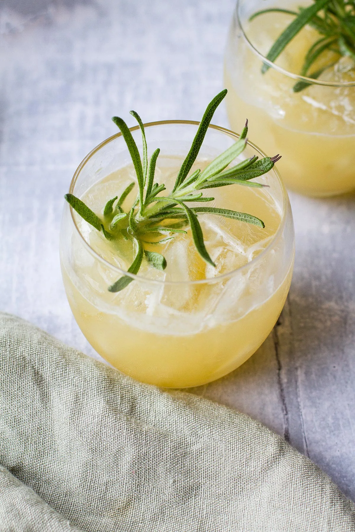 Round glass filled with a whiskey drink and garnished with fresh rosemary.