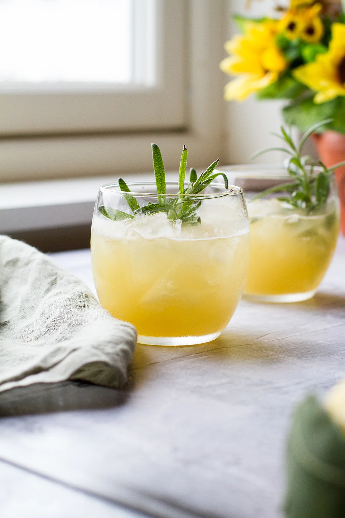 Two glasses filled with a whiskey drink and garnished with rosemary.