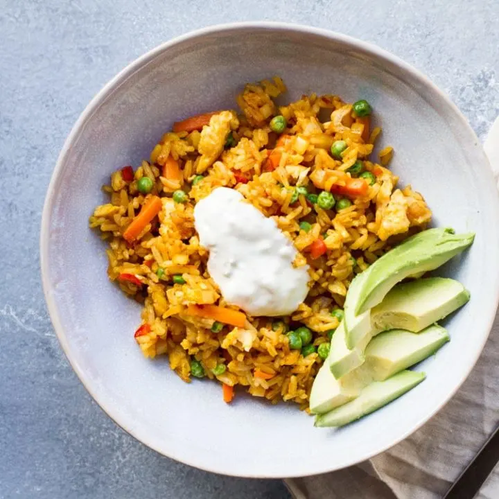 Square flatlay photo of a bowl with Mexican fried rice, avocado slices and sour cream.