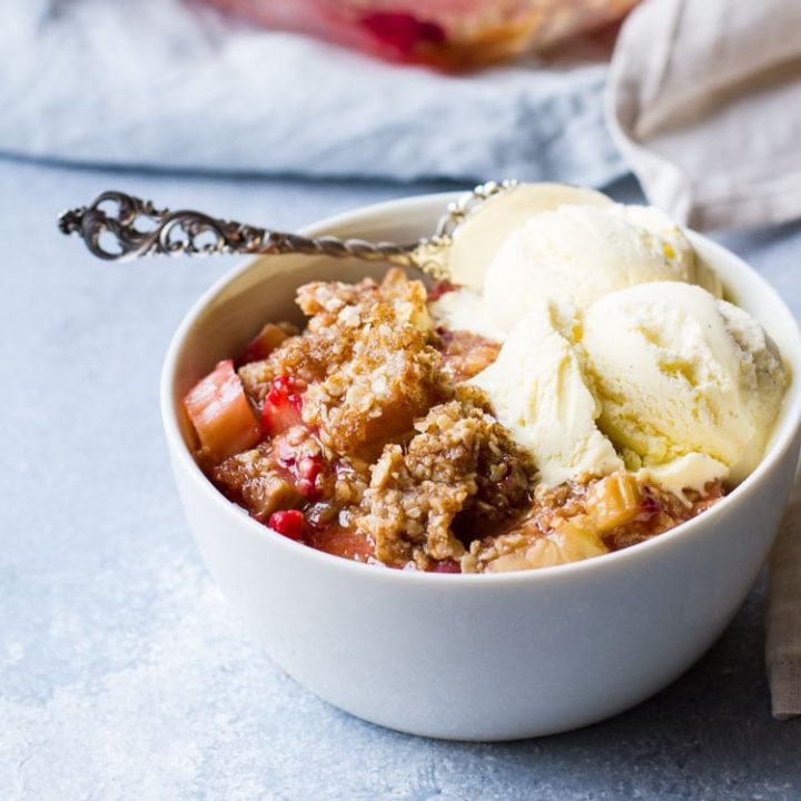 White bowl with rhubarb crisp and two scoops of vanilla ice cream.