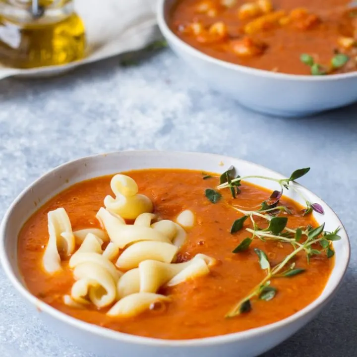 Two bowls of roasted tomato soup, pasta and fresh thyme sprig.