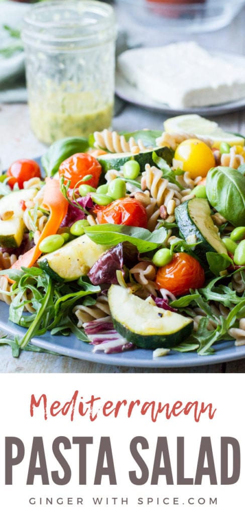 Healthy pasta salad on a dark plate, jar with pasta dressing in the background. Pinterest pin.