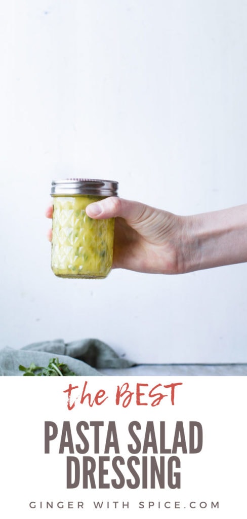 Hand holding a glass jar with a healthy pasta salad dressing. Pinterest pin.