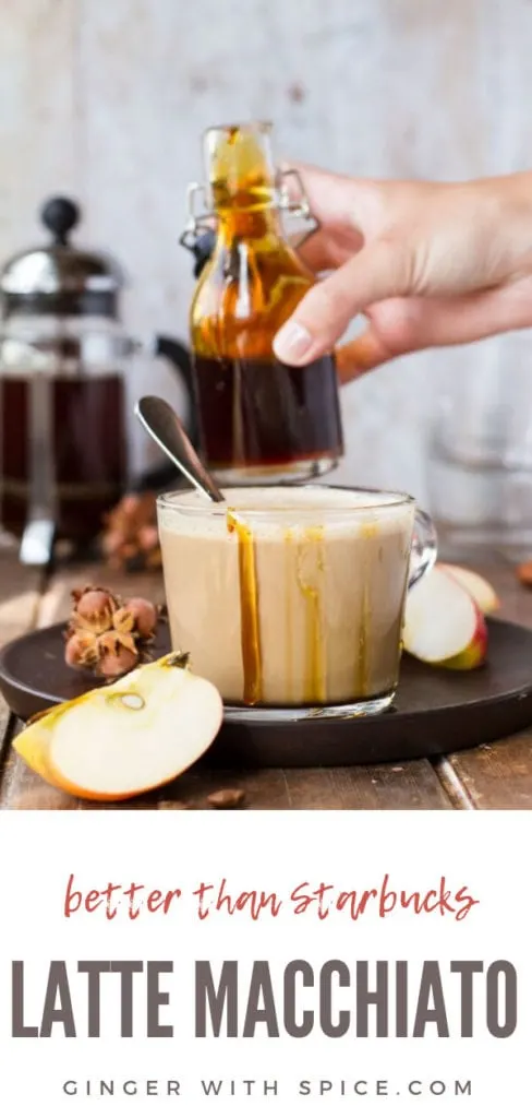 Glass cup with apple caramel latte macchiato, drizzle with caramel on the edges, hand holding glass jar with caramel in the background. Pinterest pin #2.