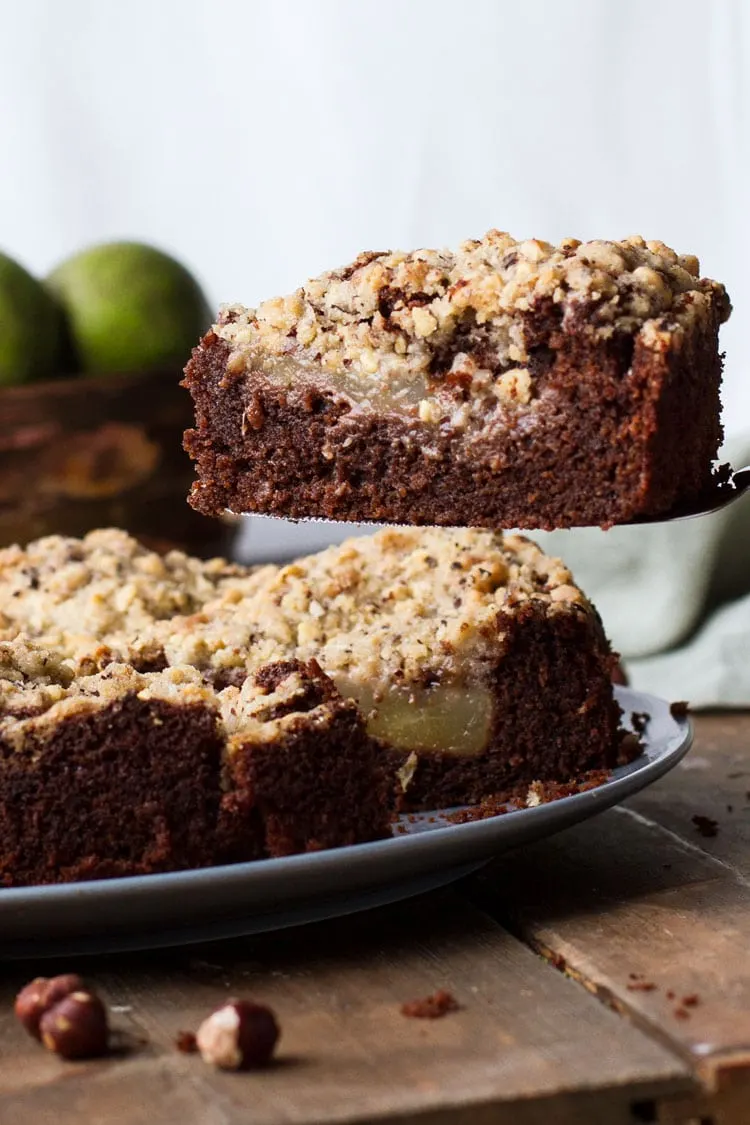 Focus on one slice of chocolate pear cake, with the whole cake in the background.