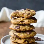 Stack of peanut butter chocolate chip cookies on a white plate, one taken a bit out of.