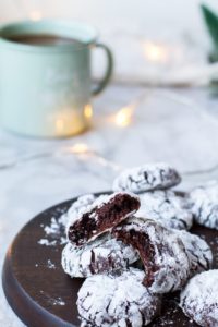 Chocolate crinkle cookies, some opened, on a wooden plate.