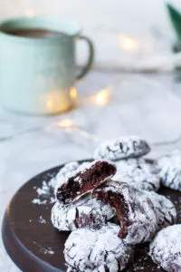 Chocolate crinkle cookies, some opened, on a wooden plate.