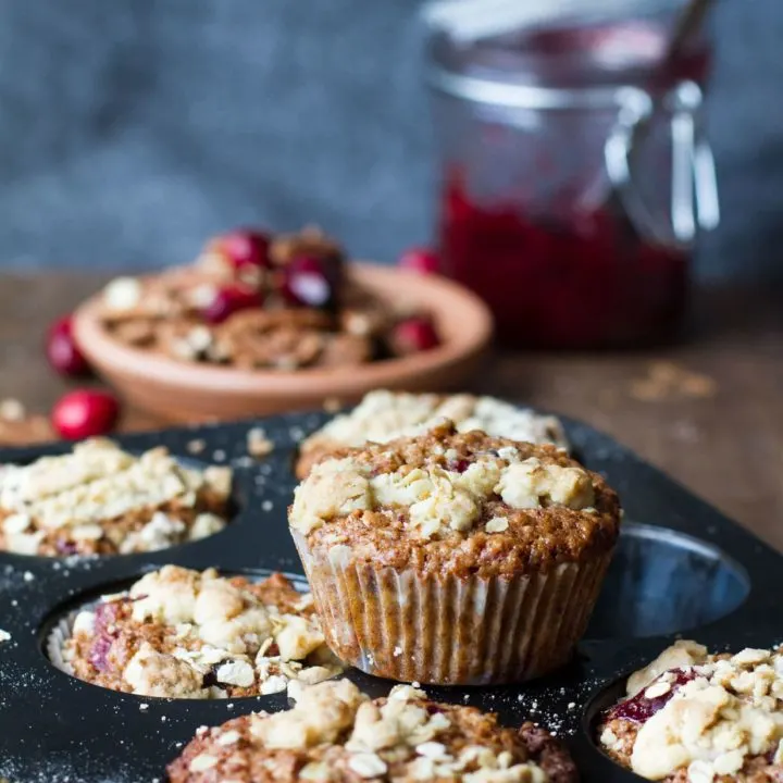 Cranberry sauce breakfast muffins on a muffin tin. Cranberry sauce in the background.