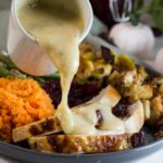 Pouring gravy on top of complete Thanksgiving meal, including turkey breast slices.