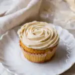 A cupcake on a white plate, with buttercream frosting shaped like a rose.