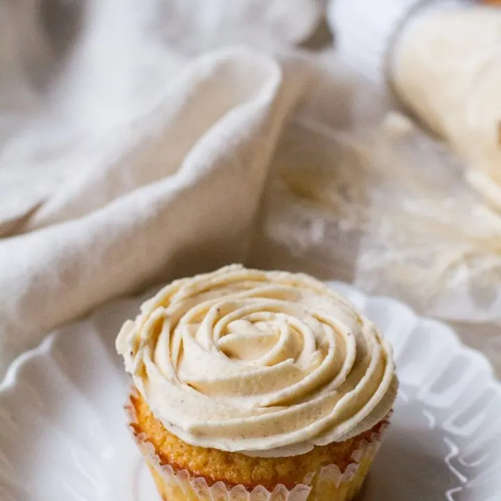 A cupcake on a white plate, with buttercream frosting shaped like a rose.