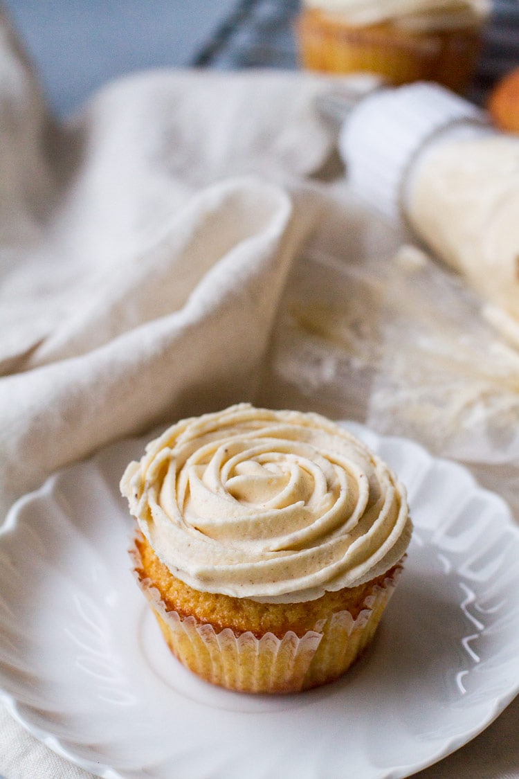 A cupcake on a white plate, with buttercream frosting shaped like a rose.