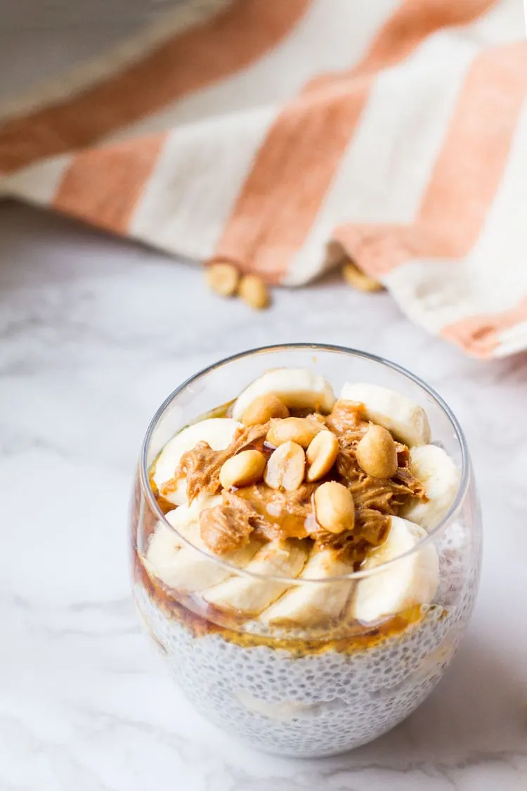 Coconut chia pudding in a round glass with toppings such as banana and peanuts.