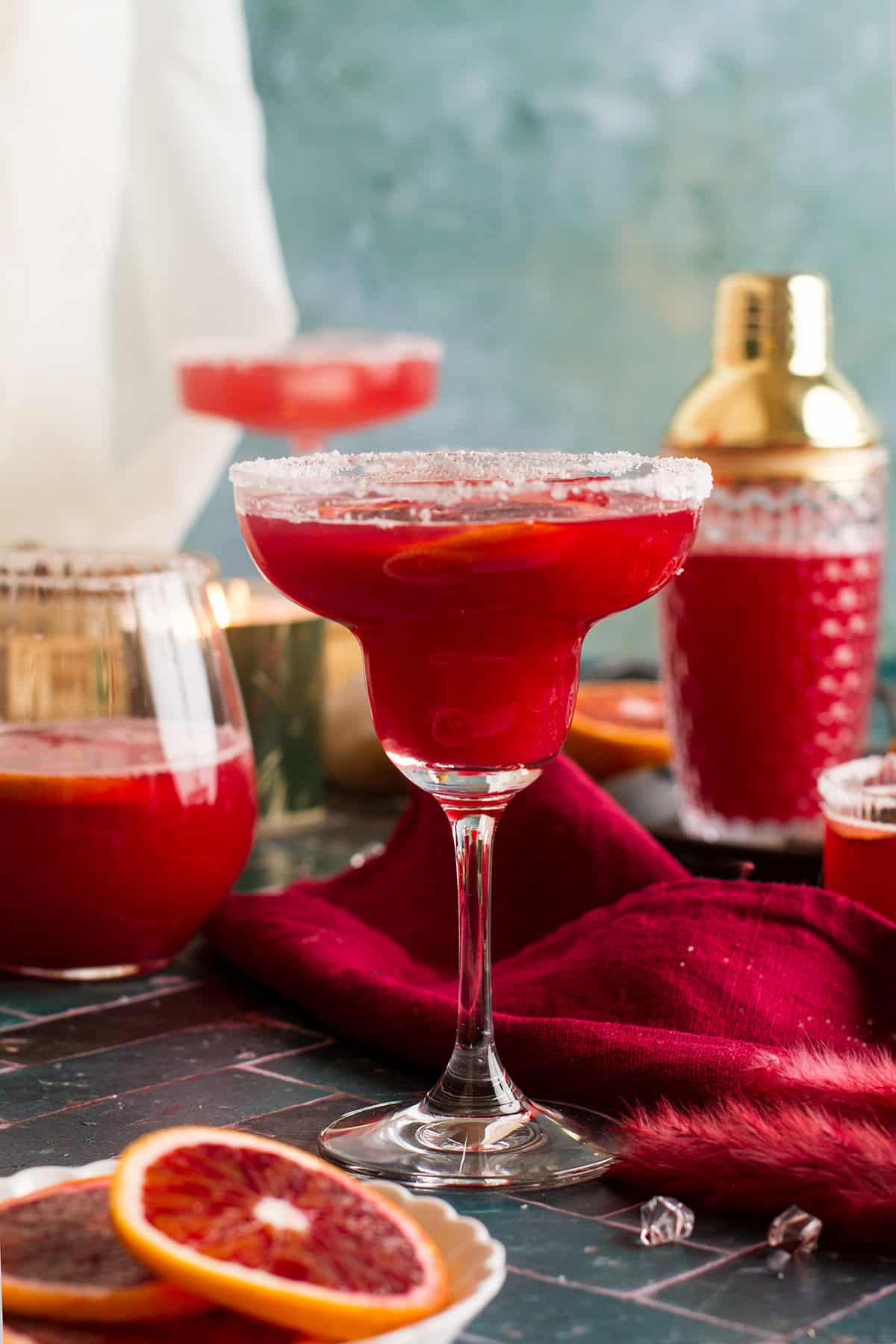 Blood orange margarita in a margarita glass. Cocktail shaker in the background. 