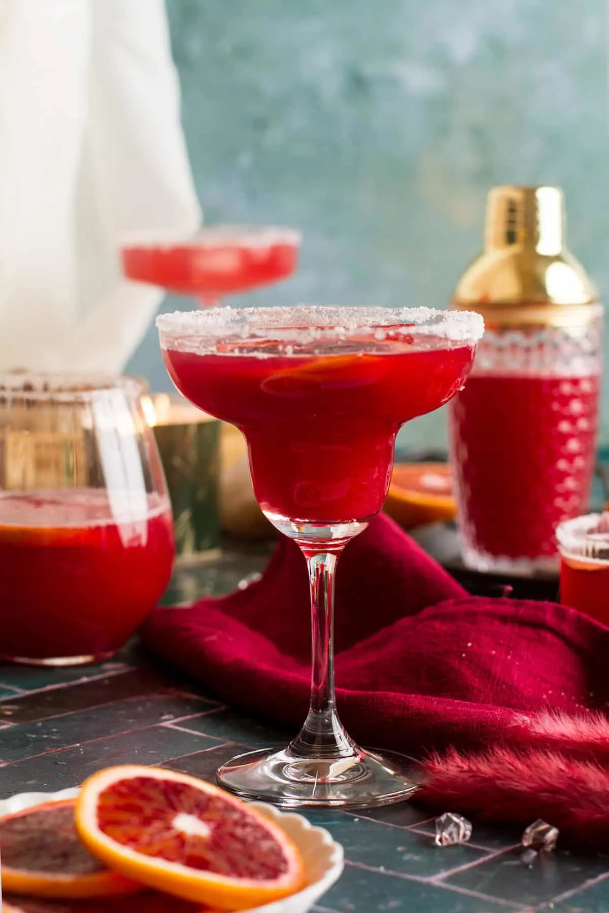 Blood orange margarita in a margarita glass. Cocktail shaker in the background. 