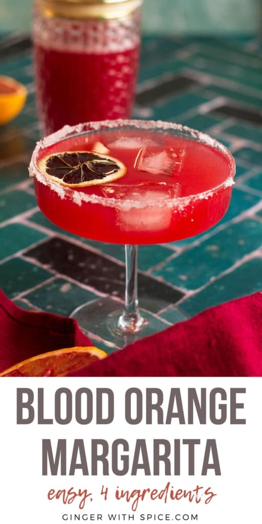 Blood or ange margarita in a coupe glass, garnished with dehydrated lime slice. Long Pinterest pin.