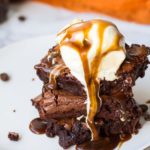 Melting ice cream scoop on top of three brownie squares. Caramel sauce on top.